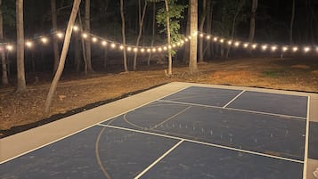 An outdoor basketball court with a wooden fence and string lights.