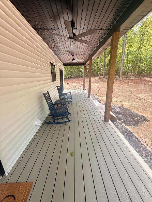 A covered porch with a ceiling fan, wooden columns, and a seating area with chairs.