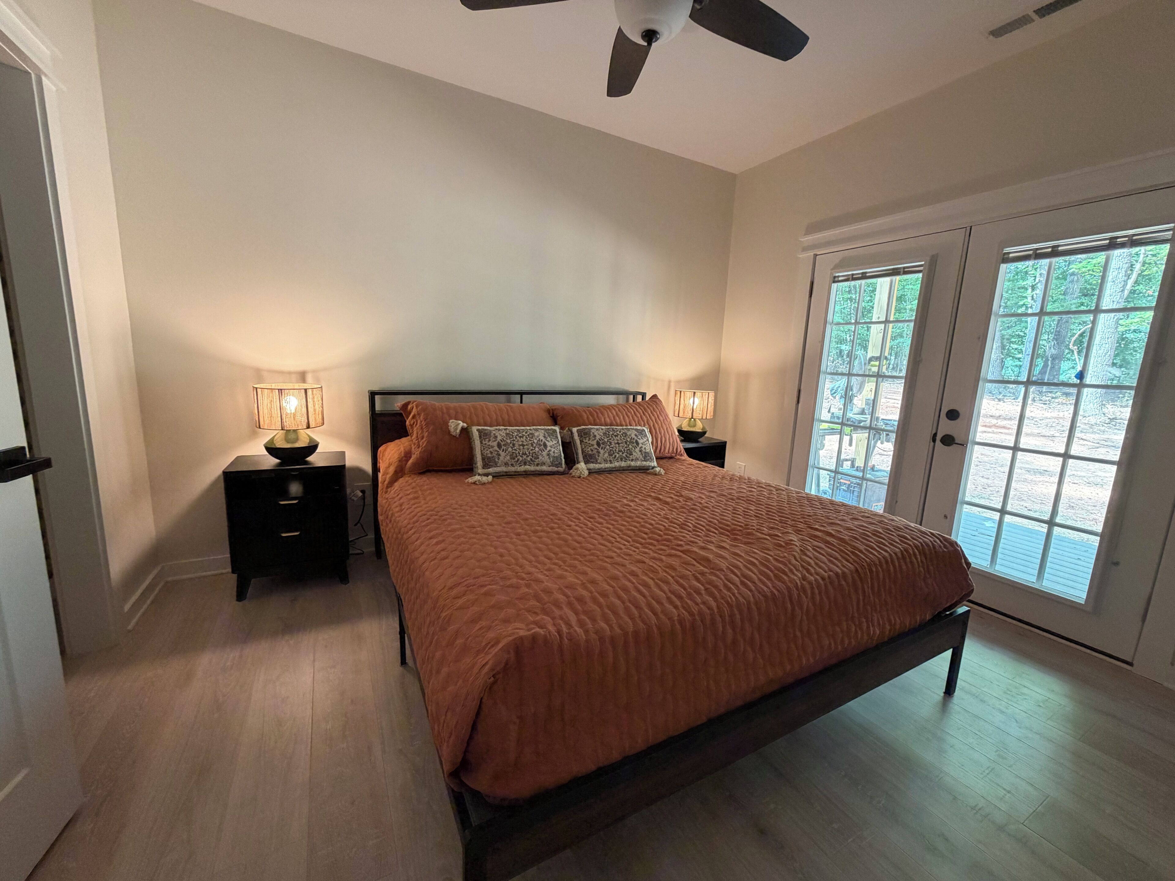 A bedroom with a bed, nightstands, a ceiling fan, and a door leading to an outdoor area.