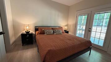 A bedroom with a bed, nightstands, a ceiling fan, and a door leading to an outdoor area.