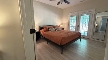 A bedroom with a bed, a ceiling fan, a nightstand, a lamp, and a large window.