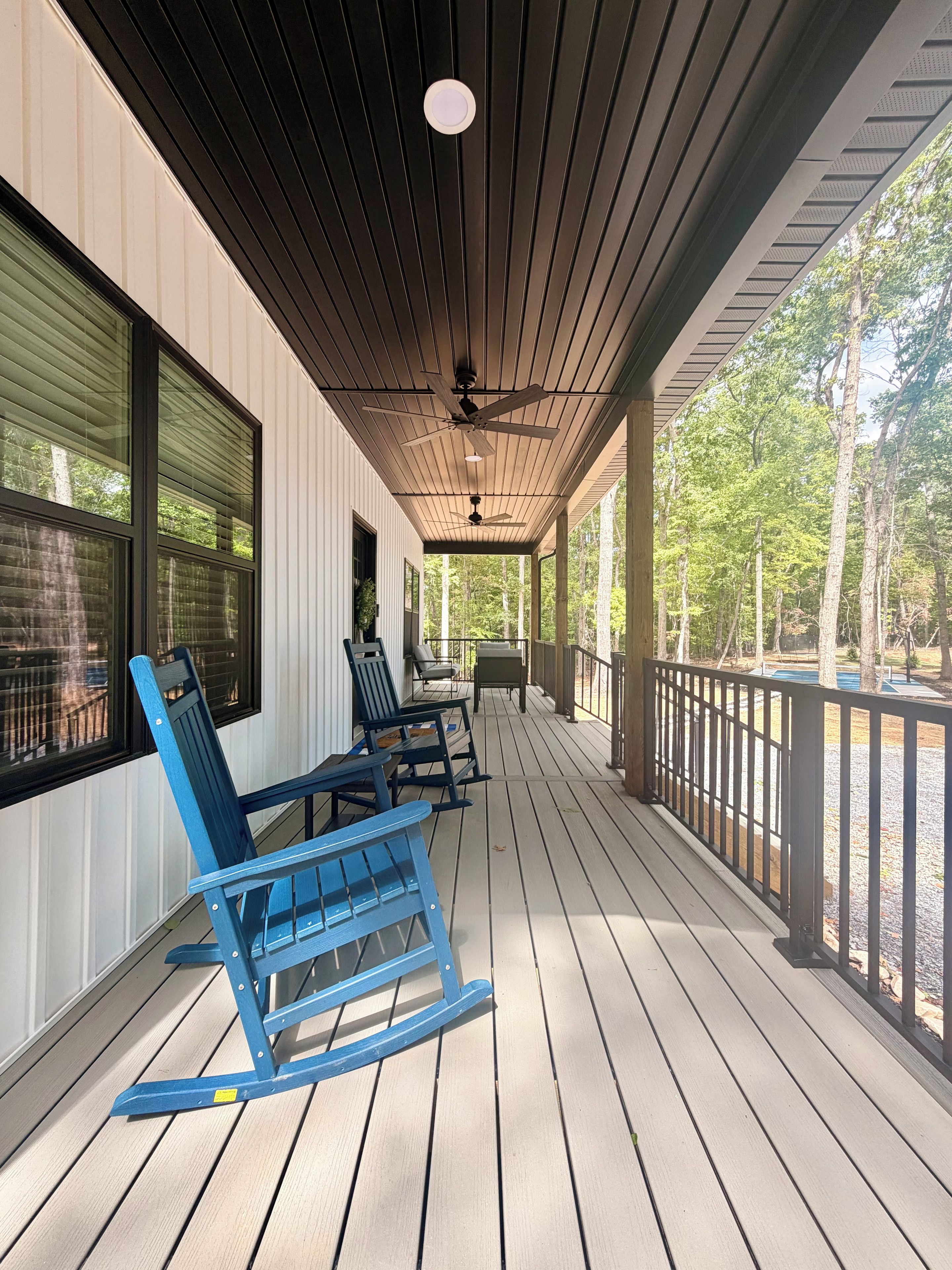 A covered porch with wooden flooring, blue rocking chairs, and a table.