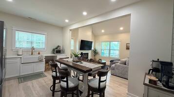 A modern kitchen with a dining area, white cabinetry, and a flat-screen TV mounted above the counter.