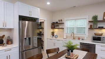 A modern kitchen with white cabinetry, a stainless steel refrigerator, a microwave, and a sink with a gold faucet.