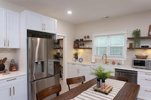 A modern kitchen with white cabinetry, a stainless steel refrigerator, a microwave, and a sink with a gold faucet.