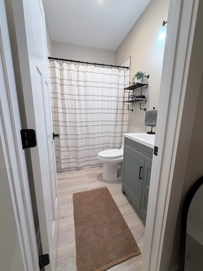 A bathroom with a shower curtain, toilet, and a shelf with toiletries.