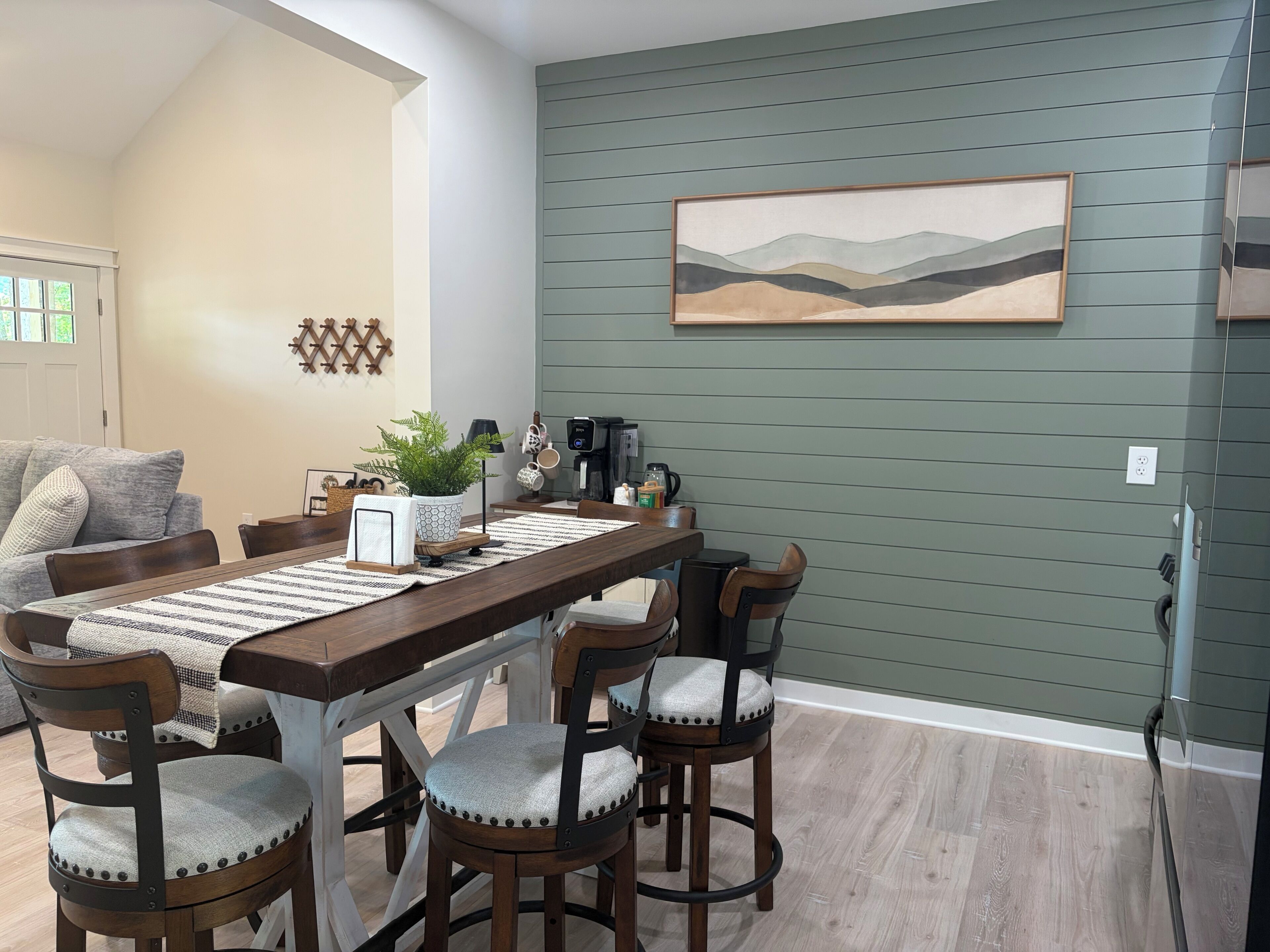 A dining area with a wooden table, chairs, a coffee machine, and a painting on the wall.