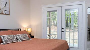A bedroom with a bed, a ceiling fan, a nightstand, a lamp, and a door leading to an outdoor area.