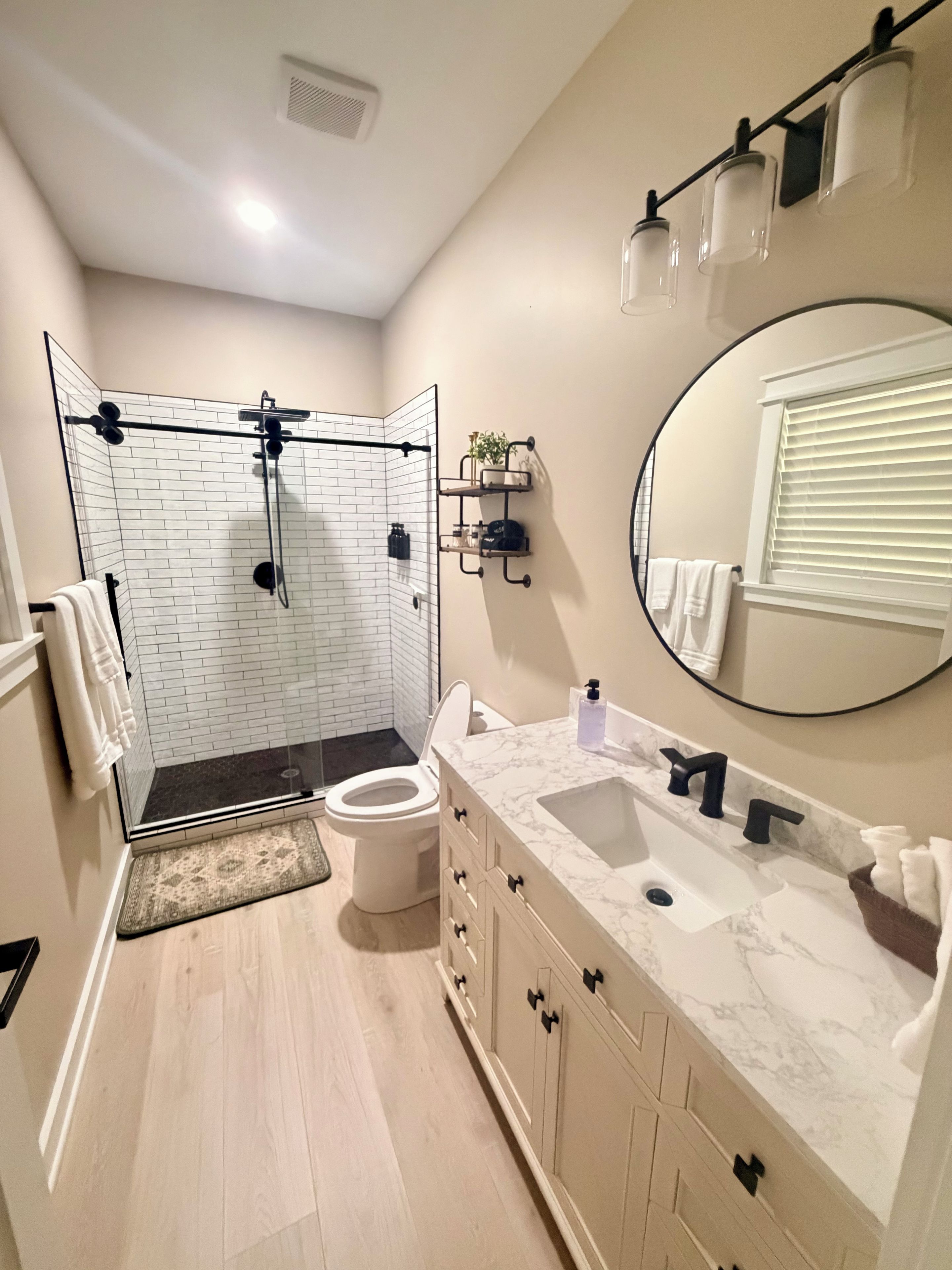 Een moderne badkamer met een douchecabine van glas, een wit toilet, een marmeren wastafel en een grote spiegel.