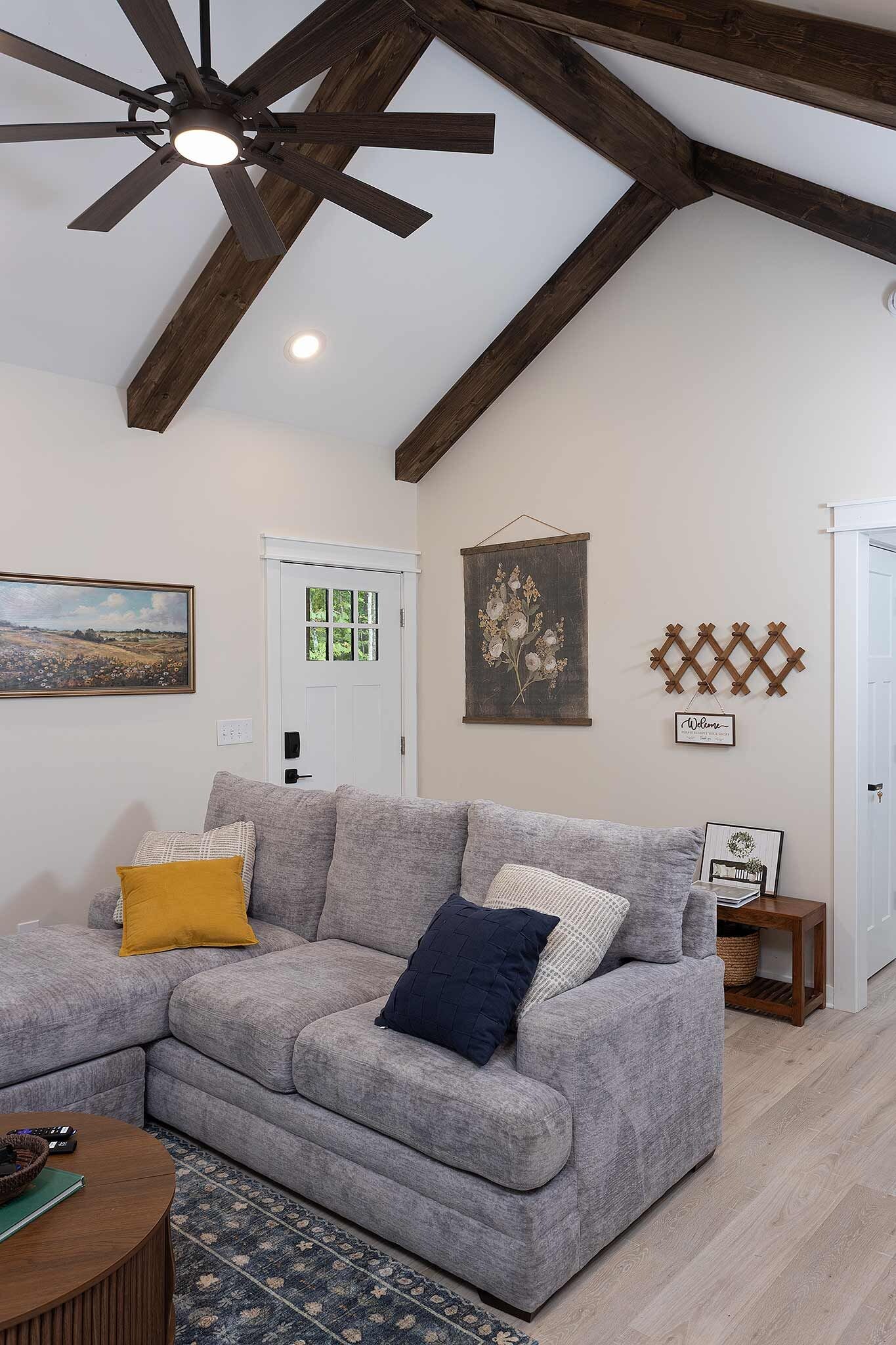 A living room with a gray sectional sofa, a ceiling fan, a door with a window, and a wall-mounted decorative item.