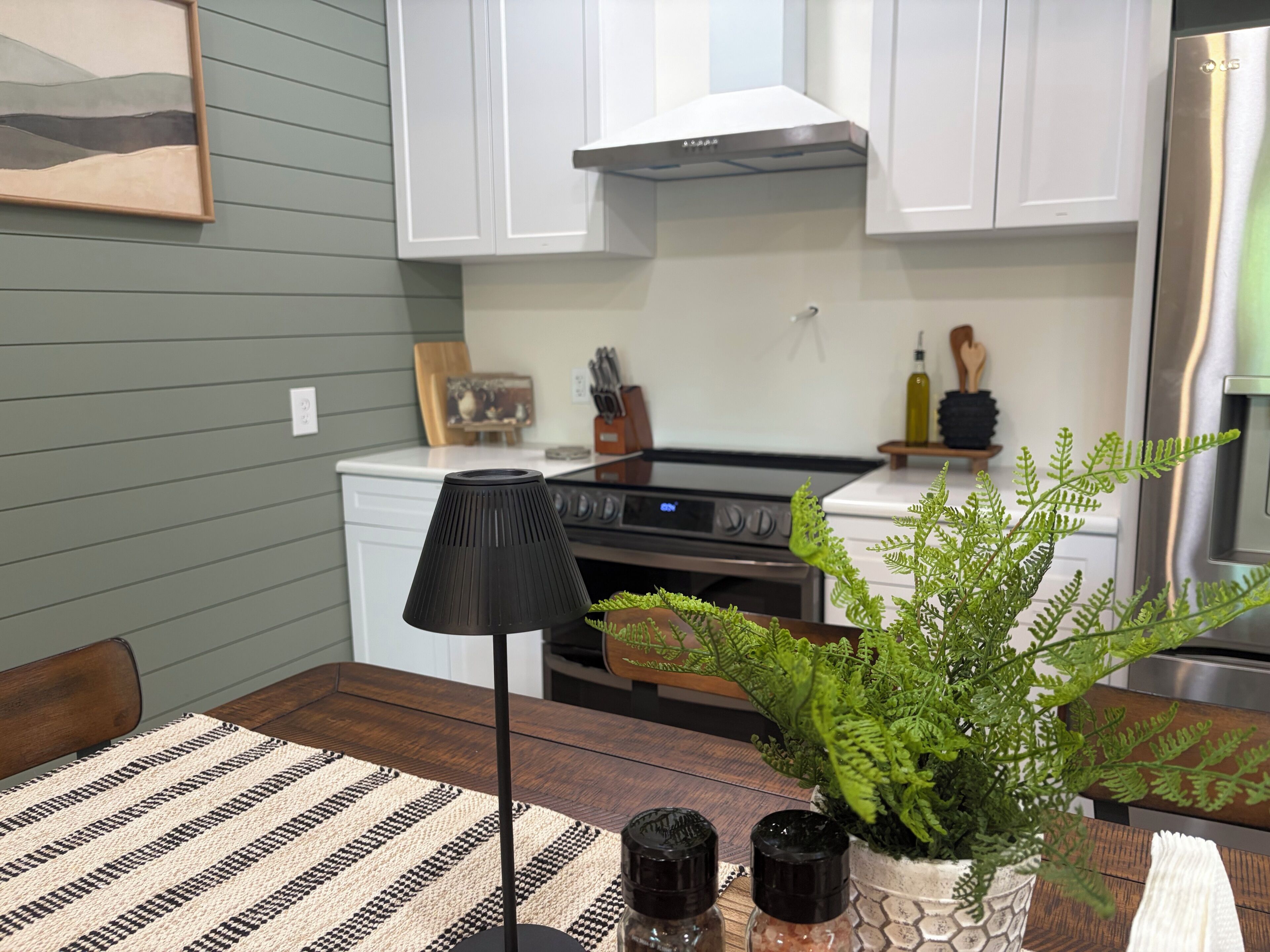 A modern kitchen with white cabinets, a stainless steel range, and a black floor lamp.