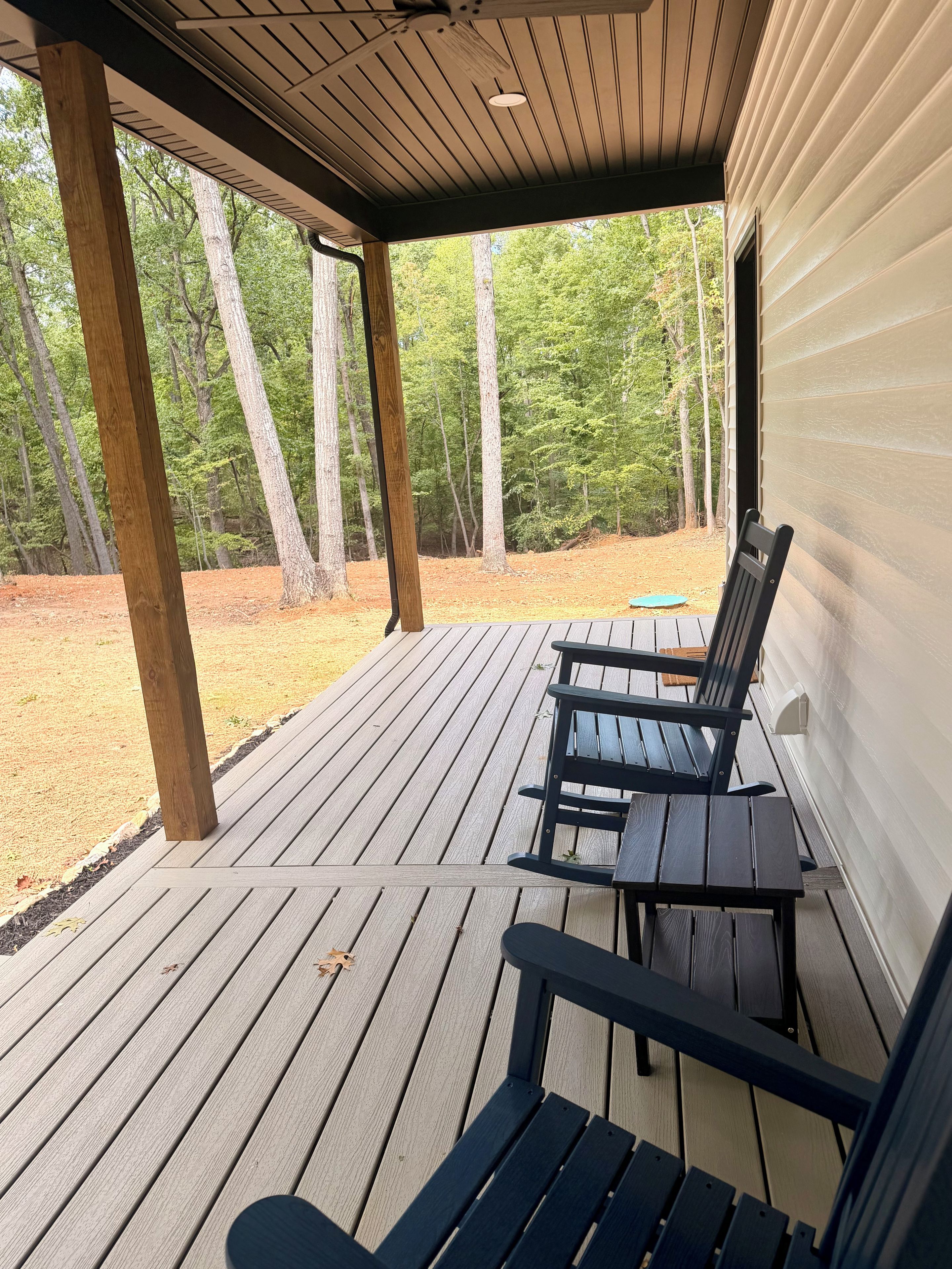 A covered outdoor area with two wooden benches, a wooden deck, and a view of a forested area.