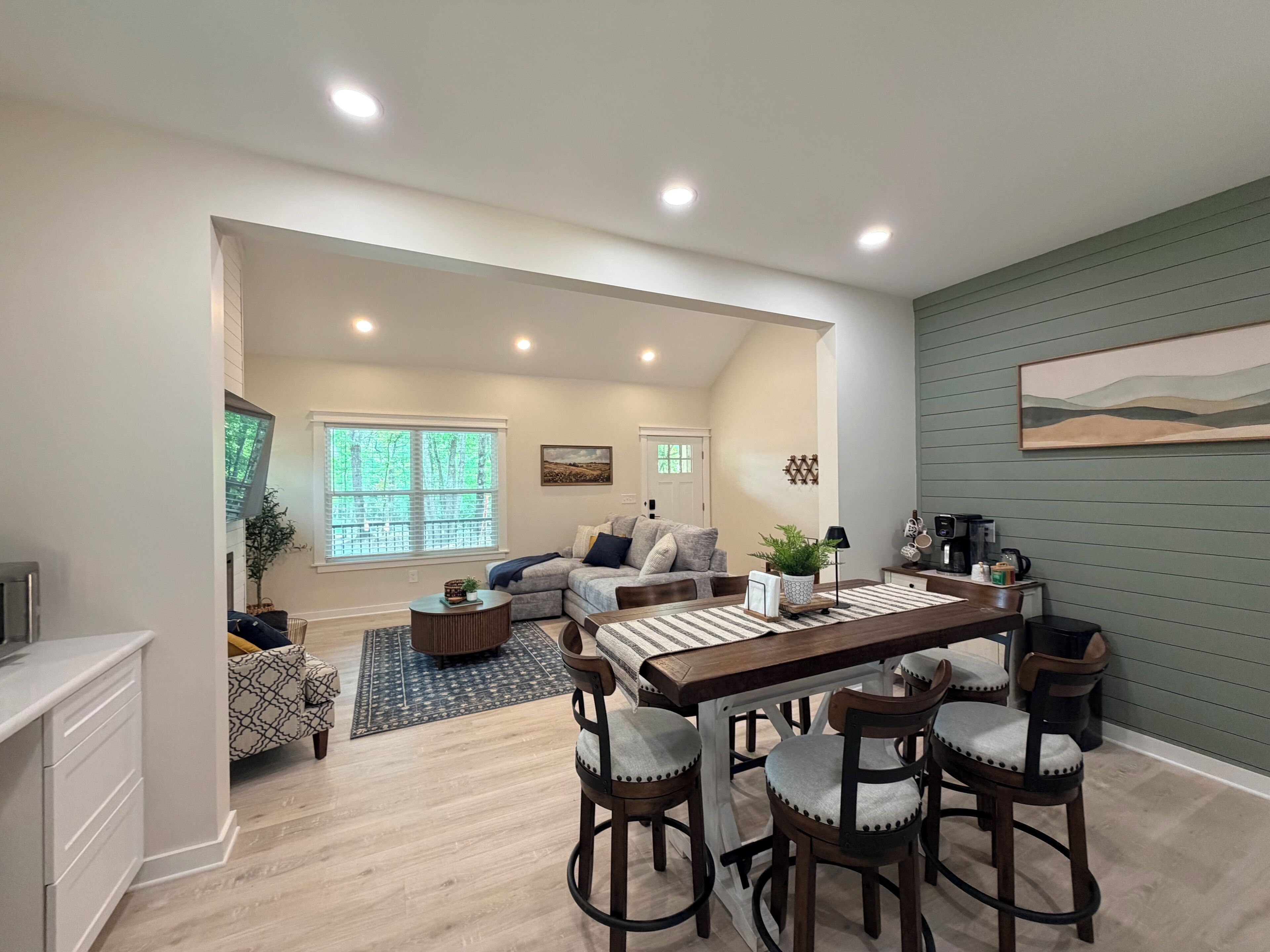 A modern living room with a dining area, a large window, and a painting on the wall.