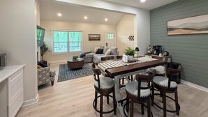 A modern living room with a dining area, a large window, and a painting on the wall.