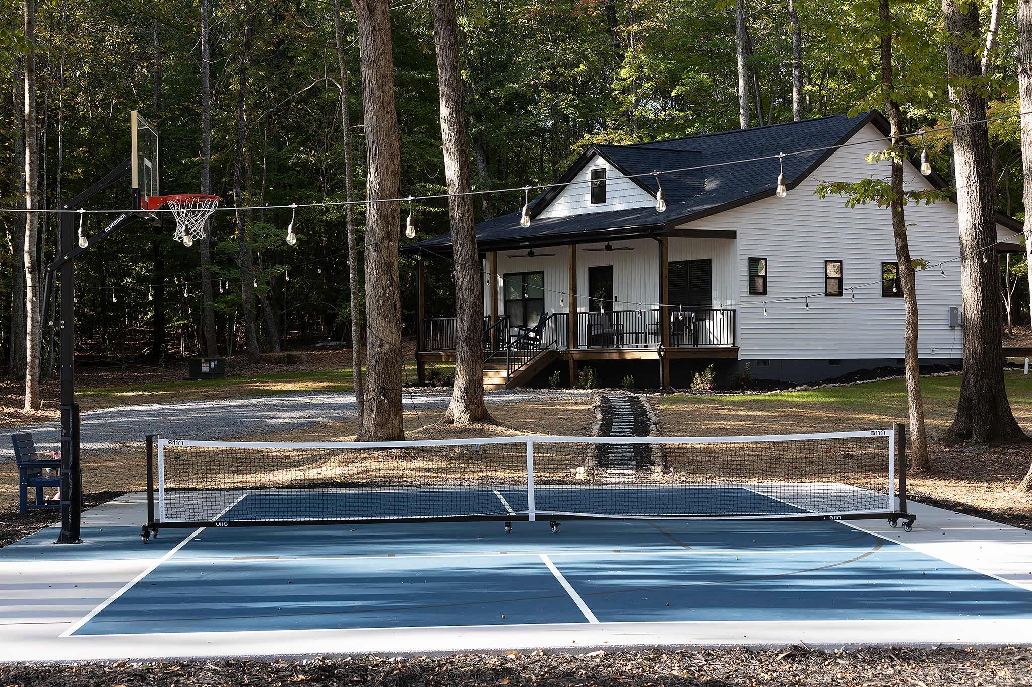 Una cancha de tenis con una red, rodeada de árboles y una casa al fondo.