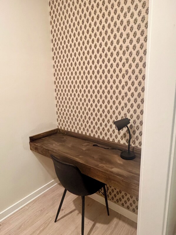 A corner workspace with a wooden desk, a black chair, and a desk lamp.