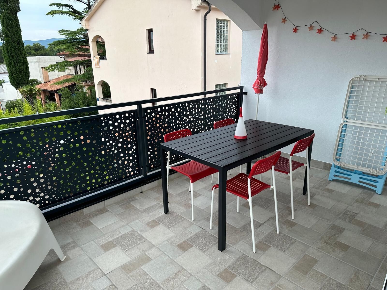 Un balcón con una mesa, sillas, una sombrilla roja y un transportín azul.