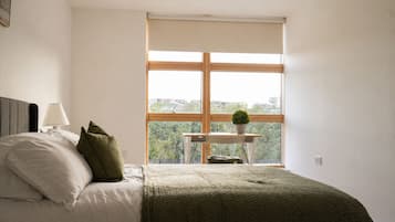 Une chambre à coucher avec un lit, une table de chevet avec une lampe, une fenêtre donnant sur un beau paysage et une petite table avec une plante.
