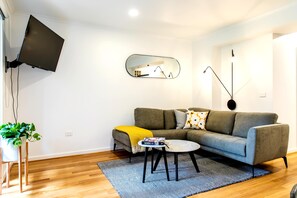 A modern living room with a grey sofa, a small coffee table, a TV mounted on the wall, and a potted plant. - Luxury spacious 2 Bedroom Fitzroy Apartment (Fitzroy)