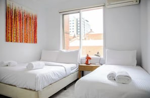 A hotel room with two beds, white bedding, a colorful abstract painting, a window with a view of buildings, and an air conditioning unit. - Luxury spacious 2 Bedroom Fitzroy Apartment (Fitzroy)