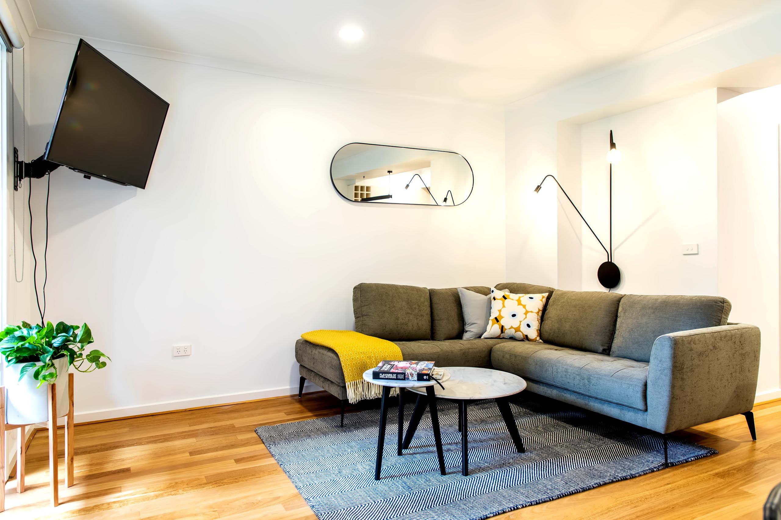 A modern living room with a grey sofa, a small coffee table, a TV mounted on the wall, and a potted plant.