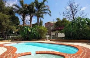 Ein Pool mit Ziegelkanten, umgeben von Grünpflanzen und einem Gebäude im Hintergrund.