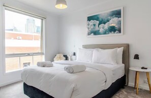 Ein Hotelzimmer mit einem großen Bett, Blick auf die Stadt und einem Bild an der Wand.