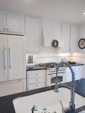 A kitchen with white cabinets, a gas stove, and a stainless steel sink. - Venice Canals Beach House (Los Angeles)
