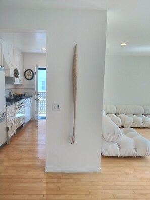A modern kitchen with white cabinets, a wooden floor, and a large white wall with a single piece of driftwood. - Venice Canals Beach House (Los Angeles)
