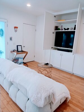 Ein Zimmer mit einer Couch, einem Fernseher auf einem Schrank und einer Schrankwand mit Regalen.