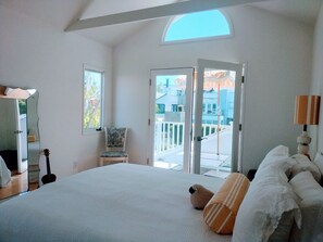 Quarto com cama grande, uma cadeira, um violão, um espelho e uma varanda com vista.