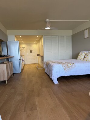 Ein Schlafzimmer mit Bett, Deckenventilator, Kleiderschrank und einer kleinen Küchenzeile.