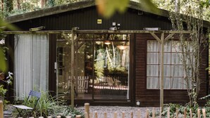 Uma cabana de madeira com varanda, rodeada por árvores e um cercado de madeira.