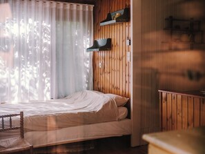 A room with a bed, wooden panel walls, a window with sheer curtains, and a shelf with items. - A cozy chalet nestled among the tall trees and birds. Pet-friendly! Great location! (Lanaken)