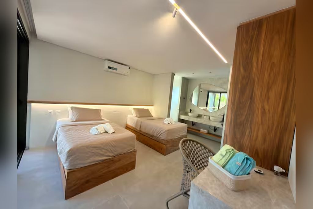 A modern hotel room with two beds, a seating area, a vanity with a mirror, and a wooden panel on the wall.