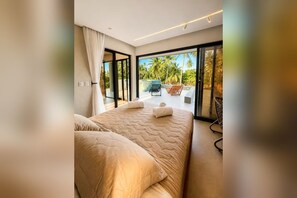A modern bedroom with a large bed, a view of the outdoors, and a balcony with seating.