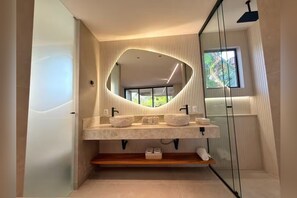 Un baño moderno con un espejo grande, dos lavamanos y una ducha.