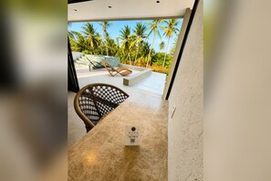 Decoração moderna com bancada de mármore, uma cadeira de vime e vista para palmeiras.