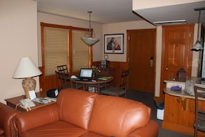 Ein Wohnzimmer mit braunem Ledersofa, einem Esstisch mit Stühlen, einer Lampe und einem gerahmten Bild an der Wand.