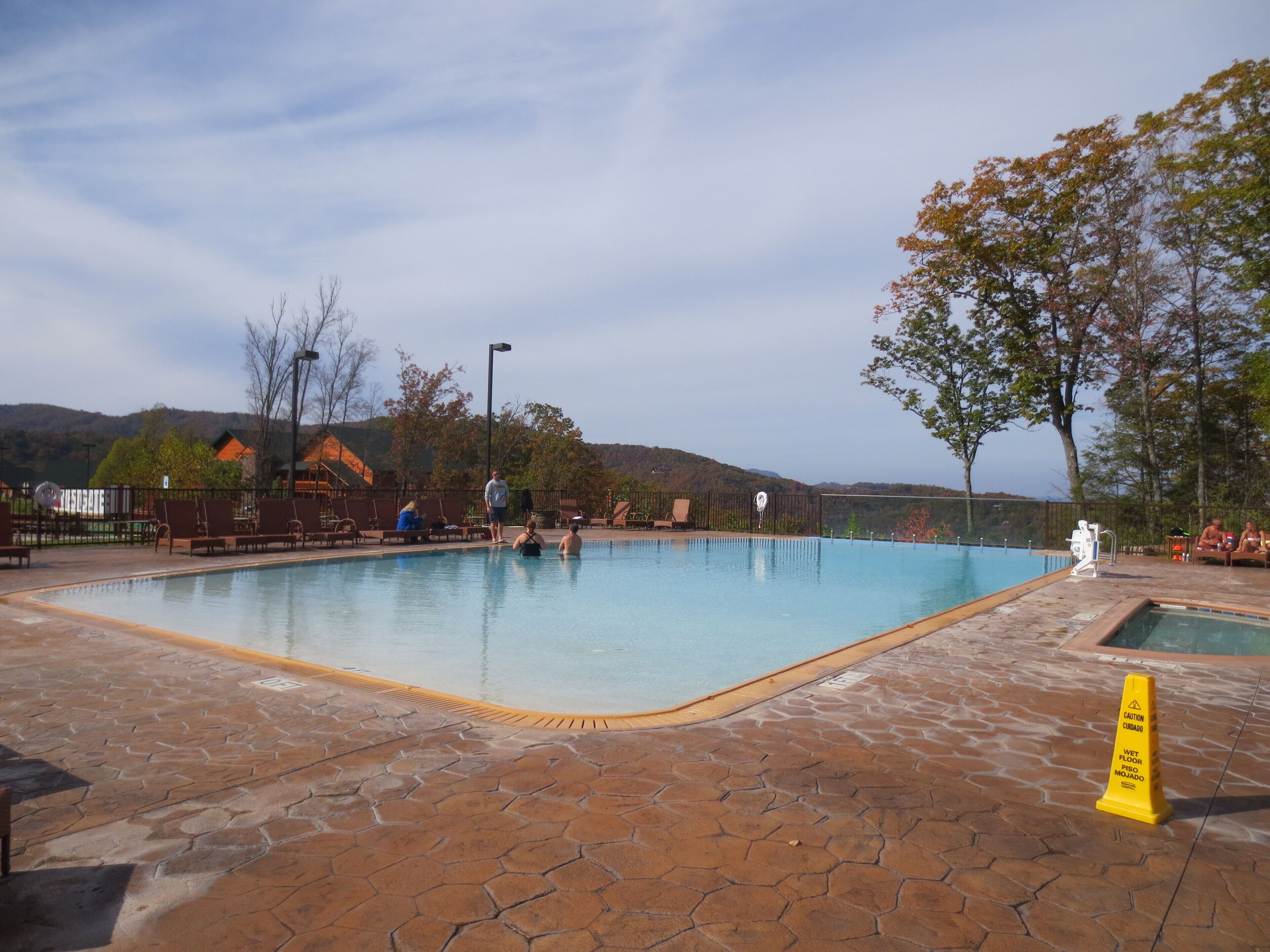 A swimming pool with a tiled deck, surrounded by chairs and a caution sign.
