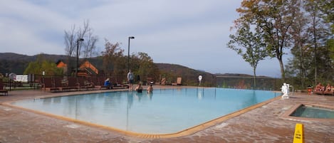 A swimming pool with a tiled deck, surrounded by chairs and a caution sign.