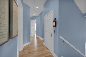 Ein Flur mit hellblauen Wänden, Holzboden und einer weißen Tür, an deren Wand ein Feuerlöscher angebracht ist.