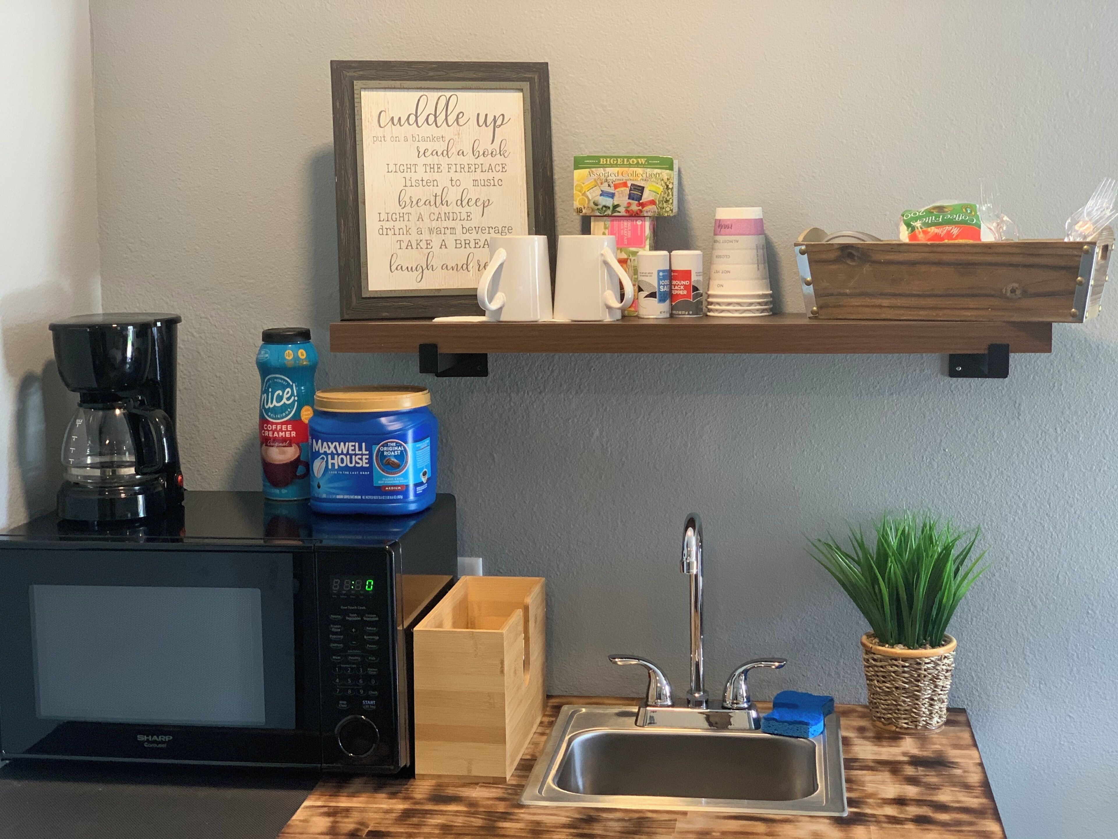 Una kitchenette con cafetera, microondas y un cartel enmarcado con consejos para relajarse.
