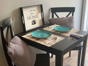 Ruokapöytä, jonka päällä on kaksi lautasesta, aterimet ja kehystetty kyltti.