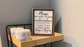 A shelf with toilet paper and a sign instructing not to flush paper towels, tissues, wipes, sanitary products, and pet supplies.