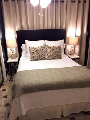 Ein Hotelzimmer mit einem großen Bett, zwei Nachttischlampen, einer Kopfteil und einem Vorhang als Hintergrund.