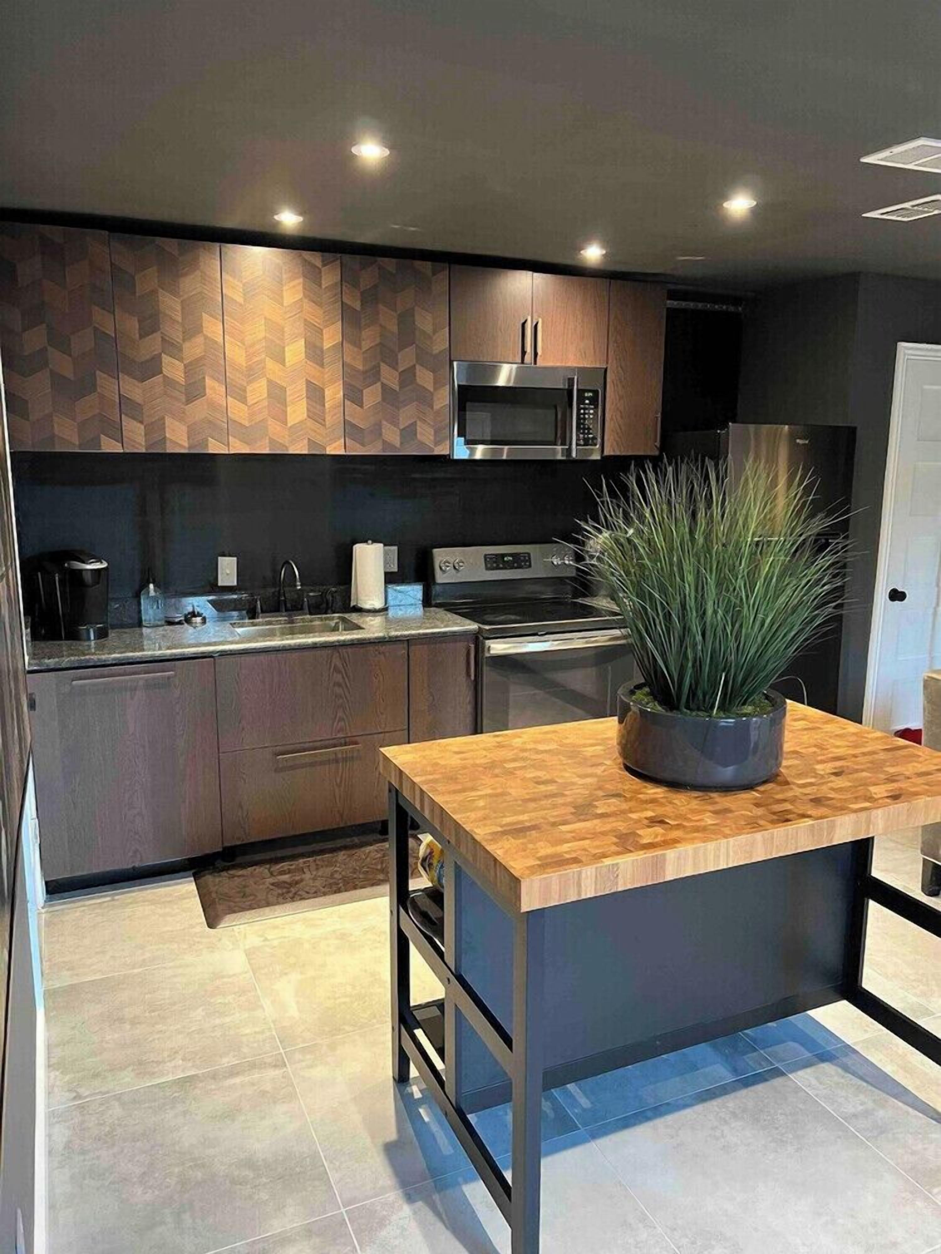 A modern kitchen with a central island, built-in appliances, and a potted plant.