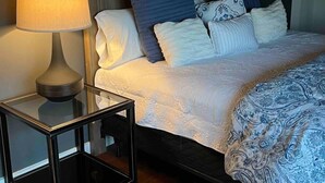 Una cama bien hecha con una colcha estampada y almohadas, una mesita de noche con una lámpara y un cabecero oscuro.