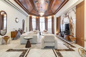 Un salón amplio con una televisión grande, asientos cómodos y un techo decorativo.