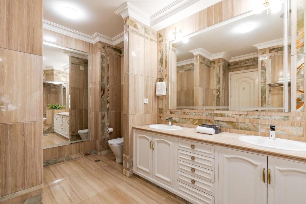 A bathroom with marble flooring, a double sink vanity, a large mirror, and a toilet.
